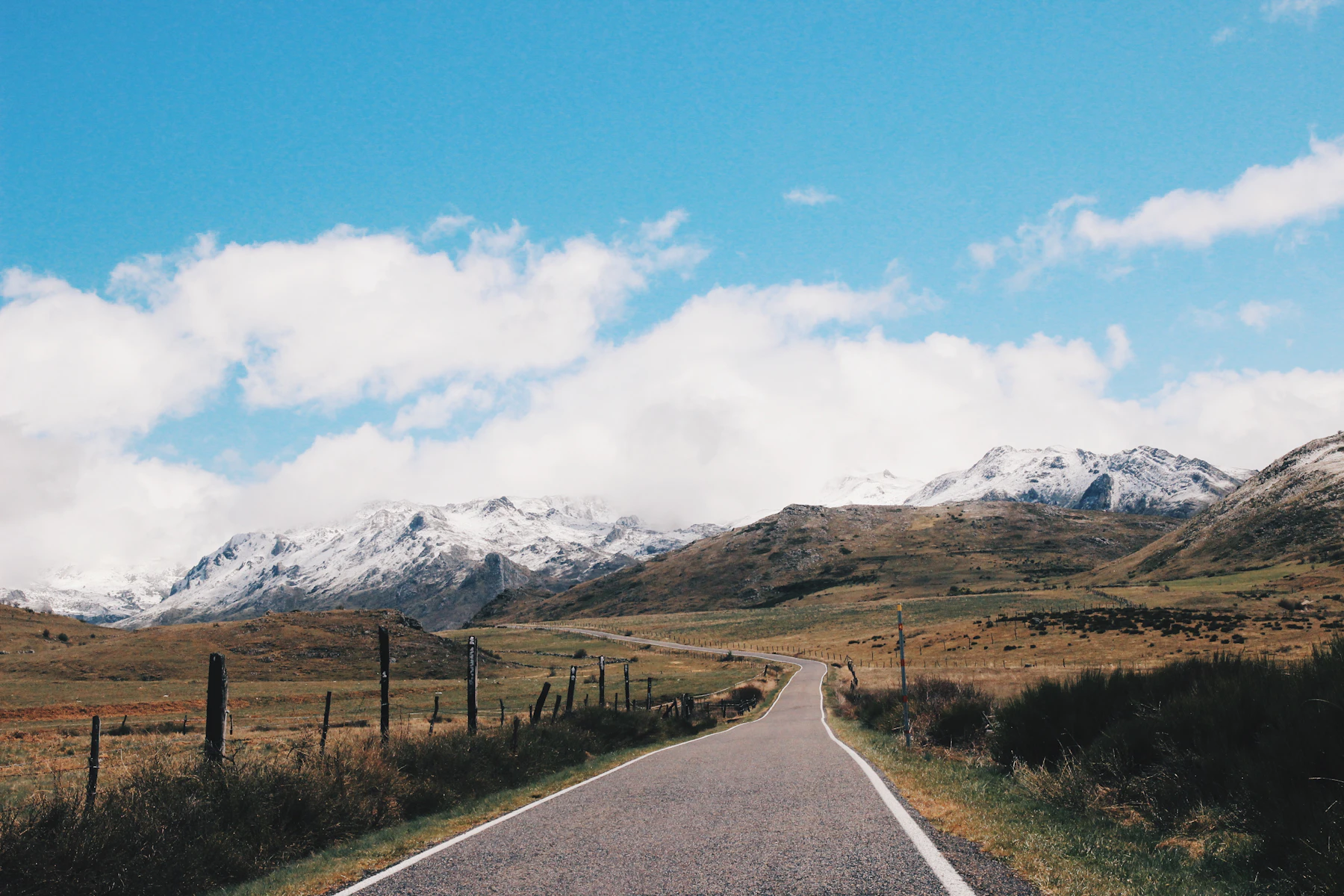 An empty road running through dry scrub toward a snow-capped sierra