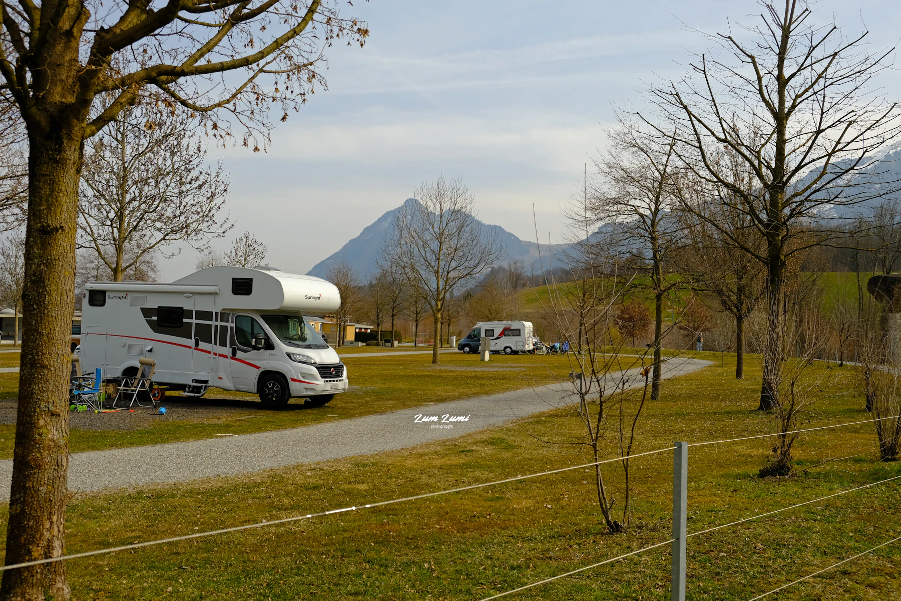 A white campervan on a grass pitch with a fence and mountains behind